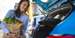Jeune femme qui range ses courses dans le coffre d'une voiture bleue